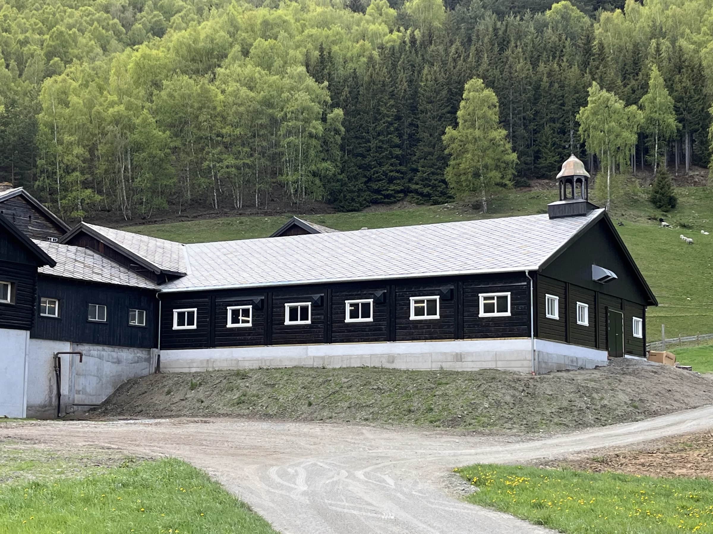 Langt driftsbygg med nytt Ottaskifer-tak og fjell i bakgrunnen, Lom
